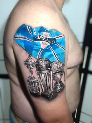 Bandeira do Grêmio colorida com taças da Libertadores e Copa do Brasil em realismo, tatuagem no braço