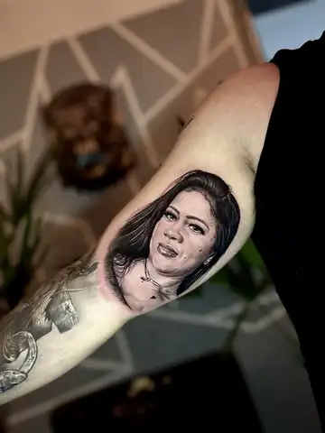 Retrato de mulher com colar, tatuagem de homenagem em realismo preto e cinza no braço interno