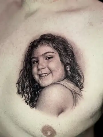 Retrato de menina sorrindo olhando por cima do ombro, tatuagem de homenagem em realismo no peito